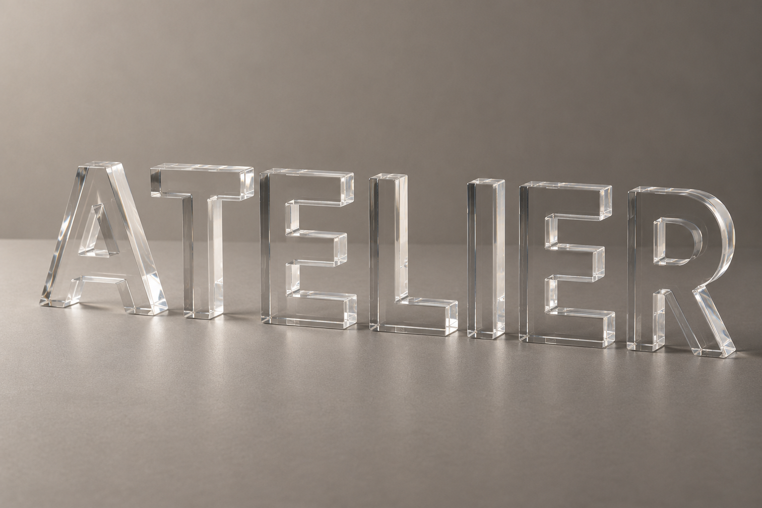 Lettres transparentes en plexiglas formant ATELIER sur un fond gris